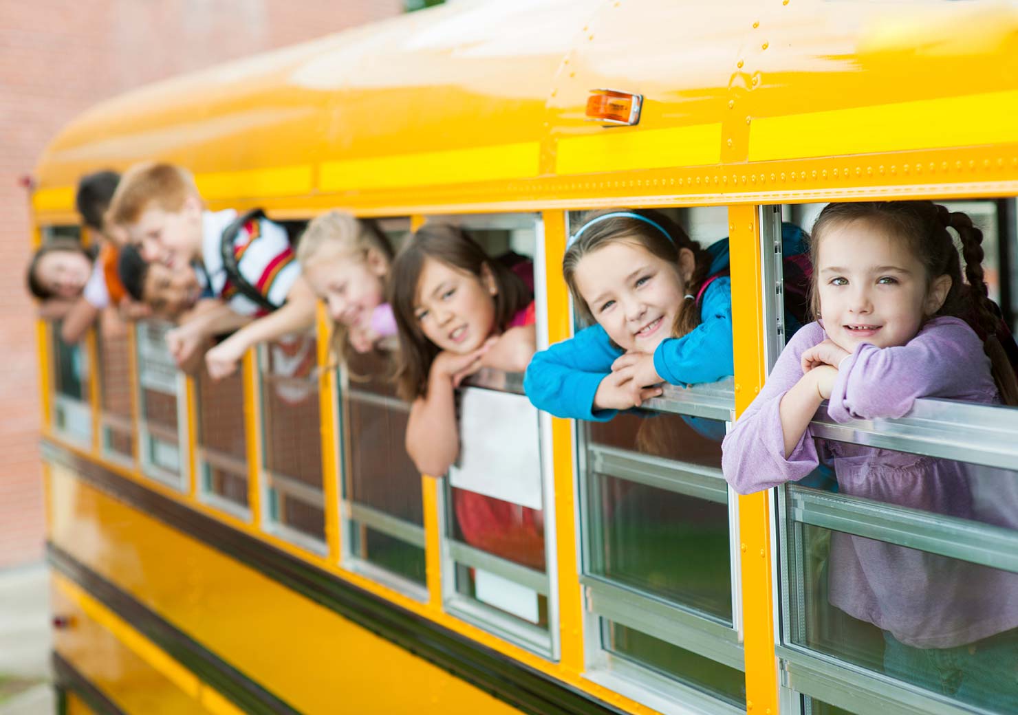 Children smiling from a school bus window, illustrating ExceleRATE’s impact on student transit safety evaluations.