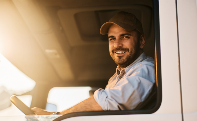 Male truck driver smiling from the cabin, representing confidence and satisfaction with safe transportation services.