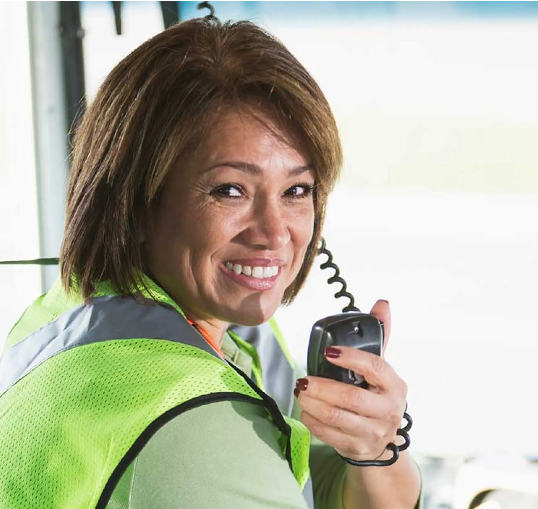 Smiling woman in a safety vest using a handheld radio, promoting professional communication and safety.