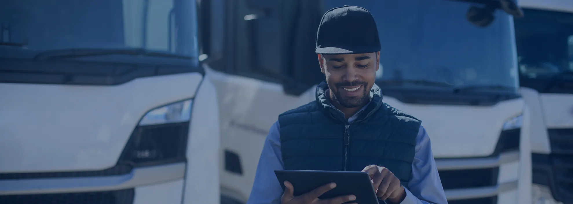 Smiling man using a tablet with trucks in the background.