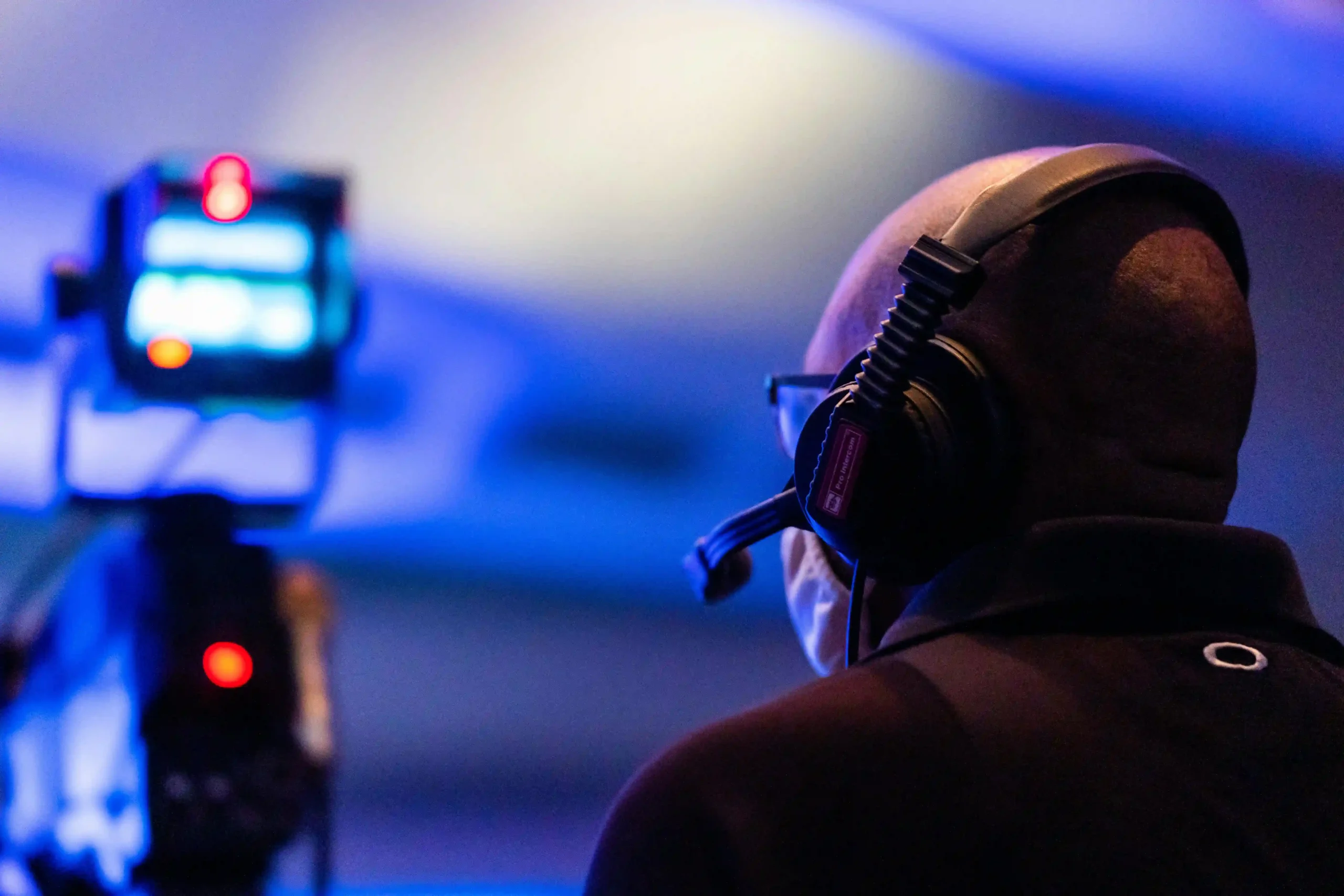 A person wearing headphones operates a camera in a blue-lit setting.