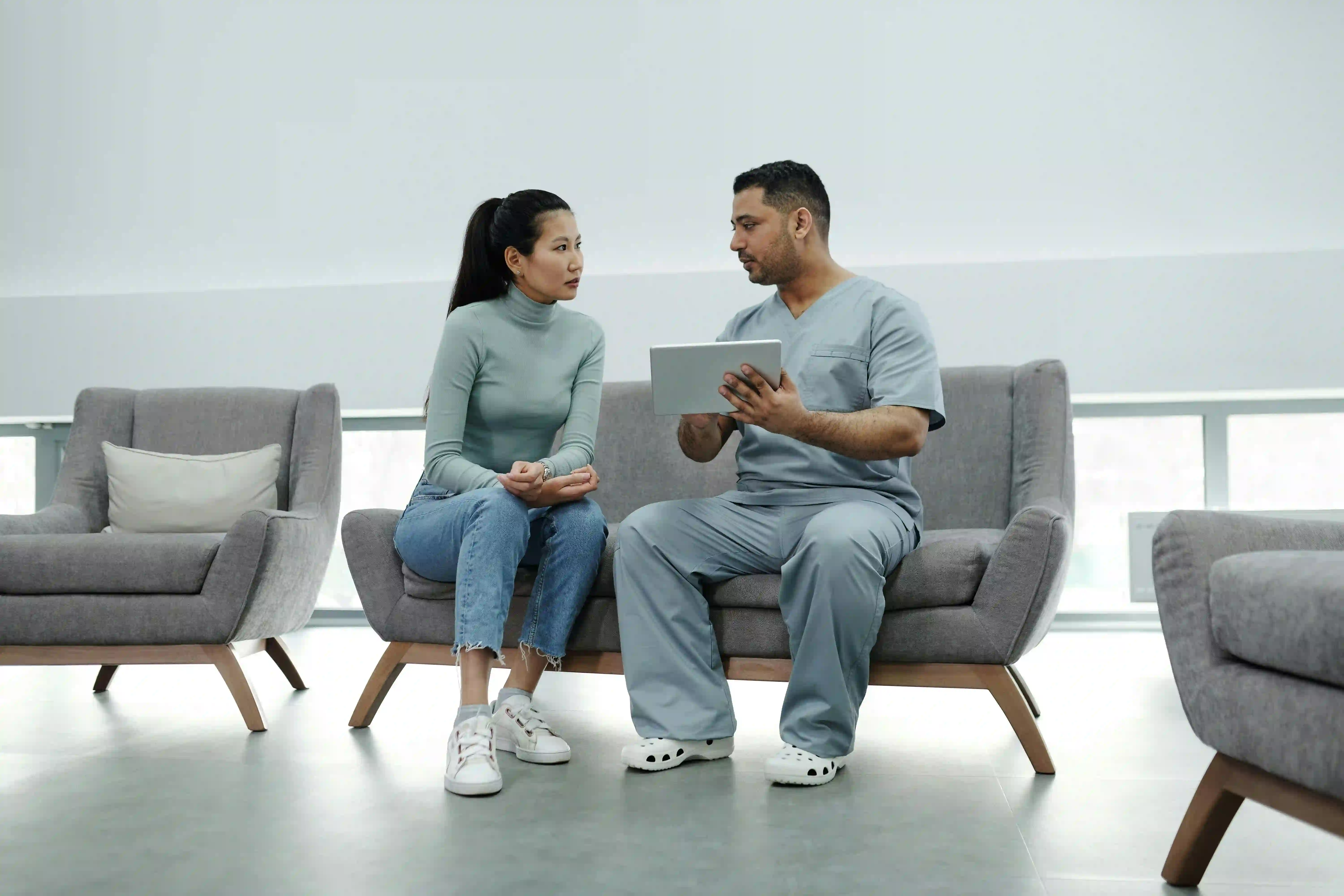 A healthcare professional sitting with a patient, reviewing information on a tablet in a modern, minimalist setting.