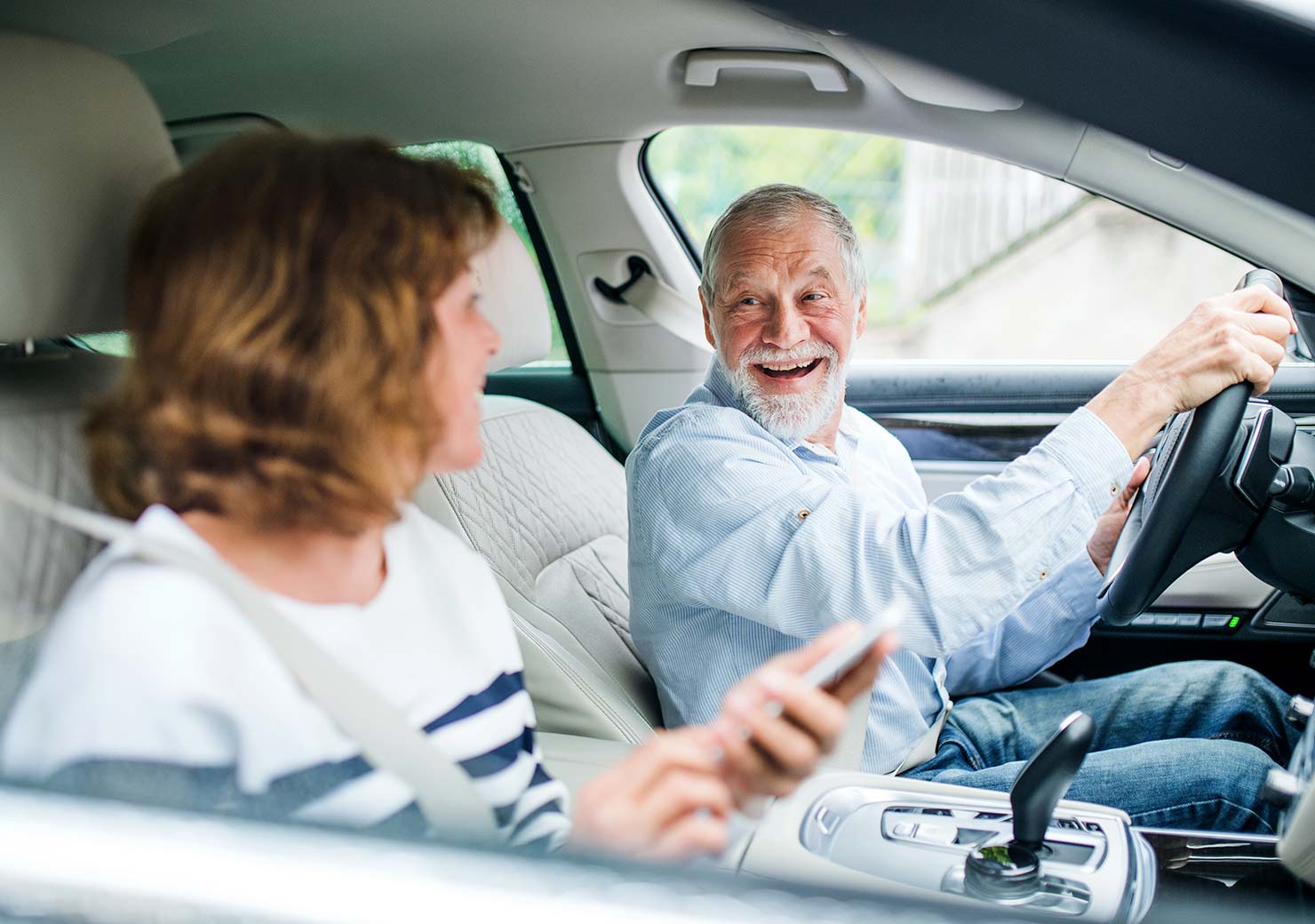 Happy senior man smiles at his wife while drivinh